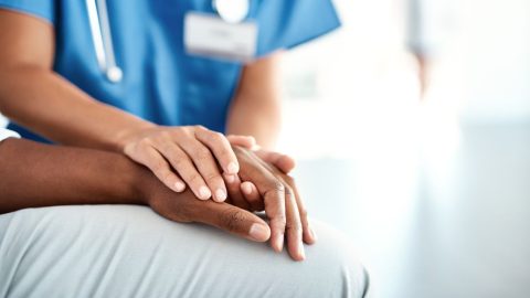 xr:d:DAE6-7f15Js:338,j:48301325295,t:23030717 Photo of a medical professional in blue holding the hand of another person.