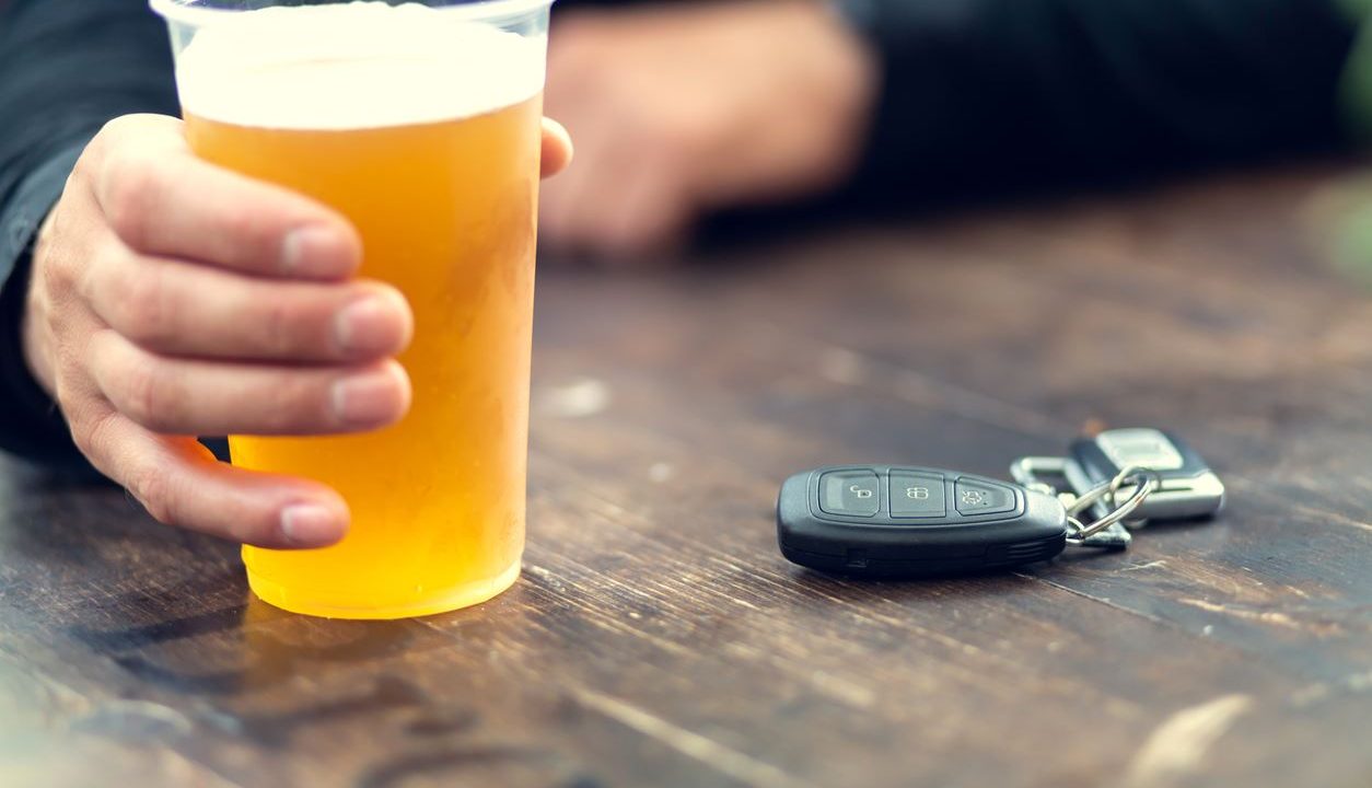 person with alcoholic beverage and car keys on table