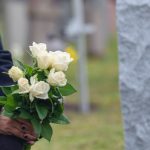 Woman kneeling with white roses before a headstone.