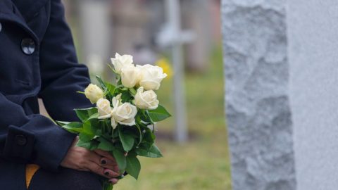 xr:d:DAE6-7f15Js:266,j:40498651806,t:22110920 Woman kneeling with white roses before a headstone.